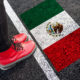 a woman standing next to flag of Mexico a woman with a boots standing on asphalt next to flag of Mexico and border
